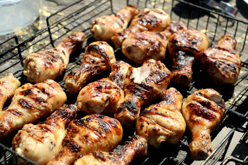 This image features a batch of grilled chicken drumsticks on an outdoor barbecue grill.